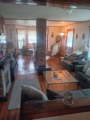 A living room with a fireplace, a sofa, a coffee table, and a dining area with a piano. - Beach 5 min walk Ocean view Spacious 3-bedroom apartment in Hyannis with AC (Barnstable)