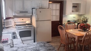 Una cocina con gabinetes blancos, estufa, horno, microondas y refrigerador. Hay una mesa de comedor con sillas y un florero con flores.