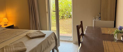 A hotel room with a bed, a table, and a view of the outside.
