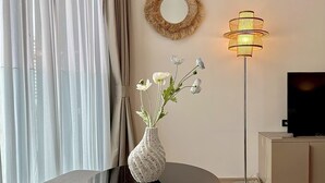 En stue med et rundt bord, en vase med blomster, en gulvlampe, et fjernsyn og et spejl monteret på væggen.