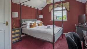 Una cama con dosel con ropa de cama blanca, un escritorio con computadora y una ventana con vista a follaje.