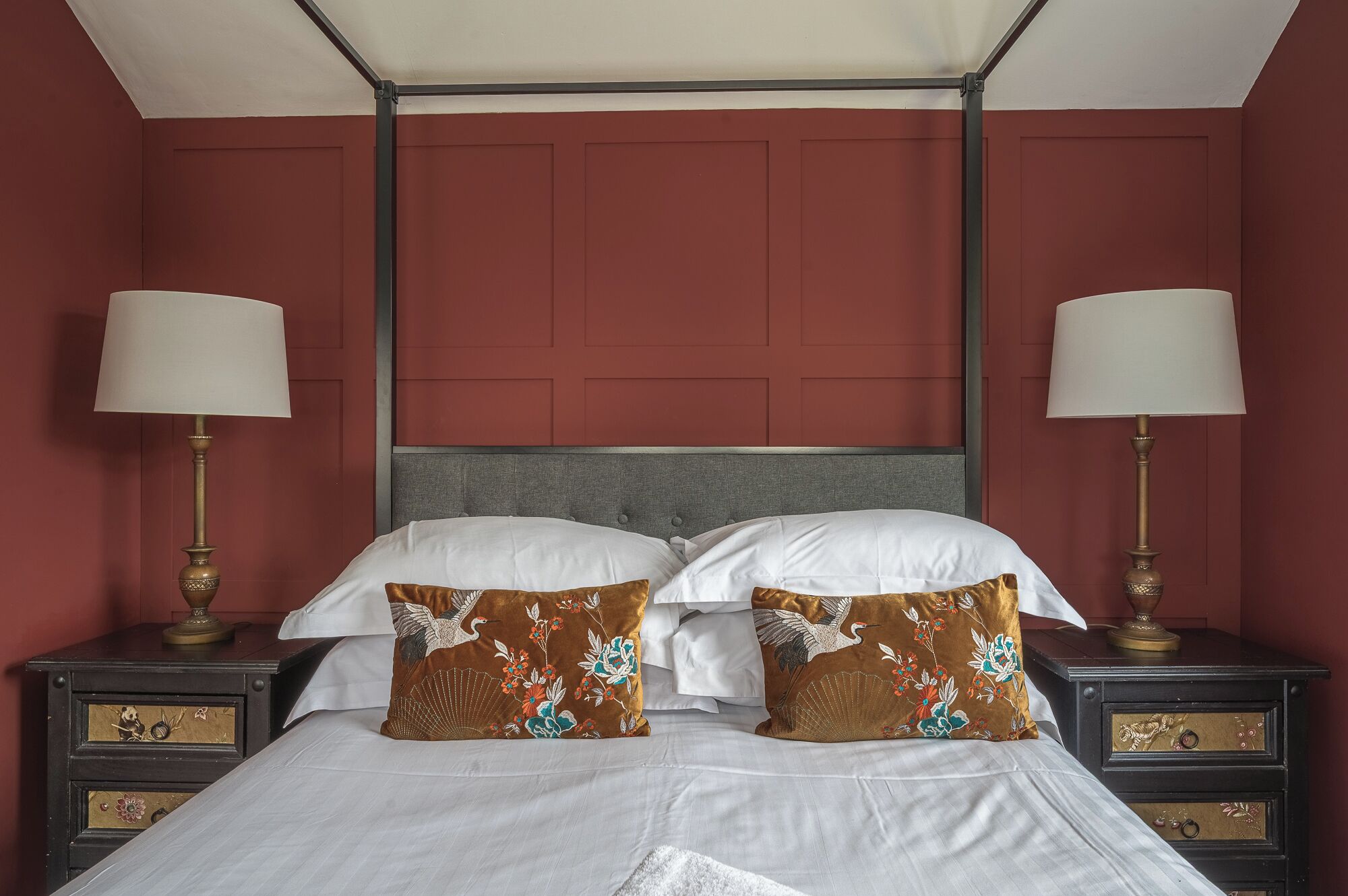 Una cama con sábanas blancas, dos almohadones decorativos, un cabecero gris y dos mesitas de noche con lámparas.