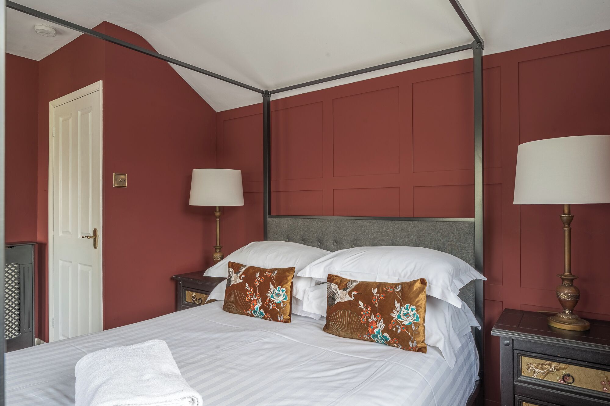 A room with a four-poster bed, two bedside lamps, a white door, and a small cabinet.