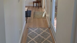 Un couloir avec un plancher en bois, un tapis à motifs, une chaise, un porte-manteau et une porte-fenêtre coulissante.