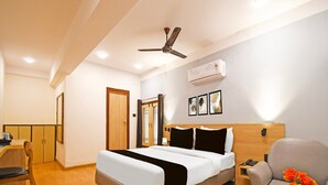 Ein Hotelzimmer mit Bett, einem Sessel, einem kleinen Tisch mit Blumen, einem Deckenventilator und einer Klimaanlage.