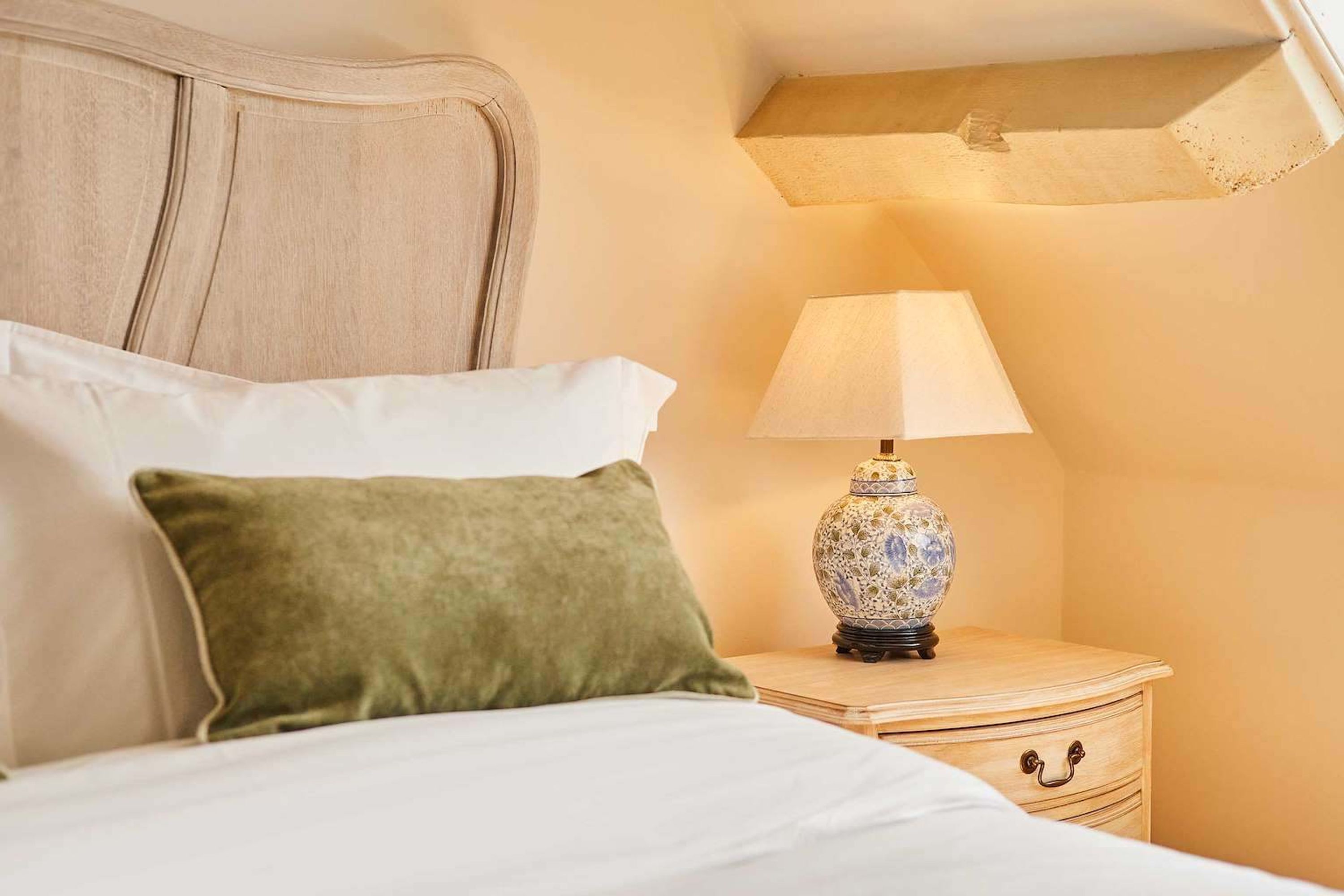 A neatly made bed with pillows, a bedside lamp, and a wooden nightstand.