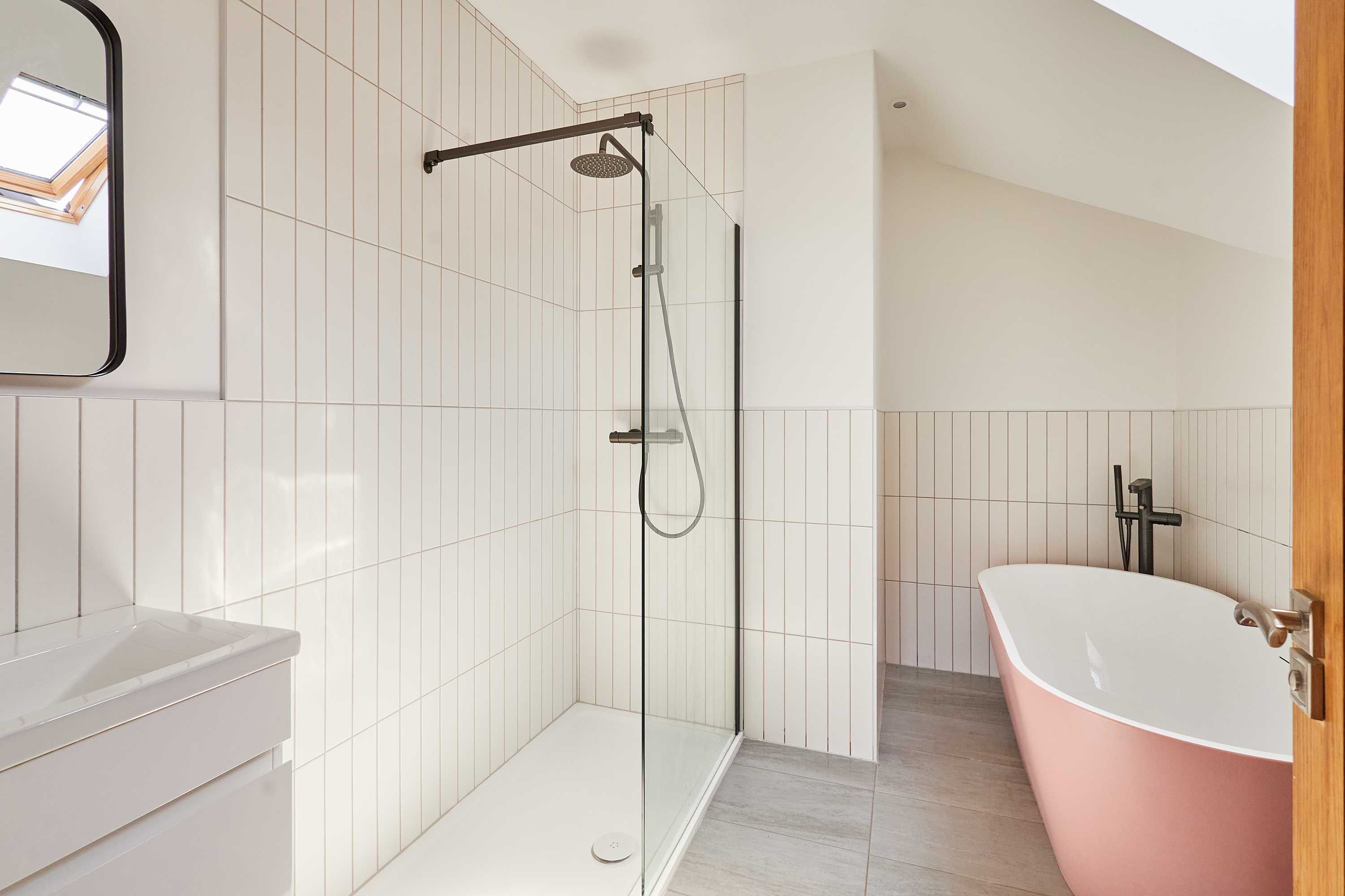 A modern bathroom with a glass-enclosed shower, a white sink, and a pink freestanding bathtub.