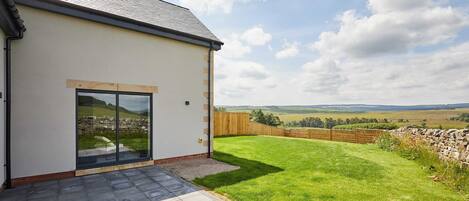 A modern house with a large glass door, a paved patio, and a view of a grassy field.
