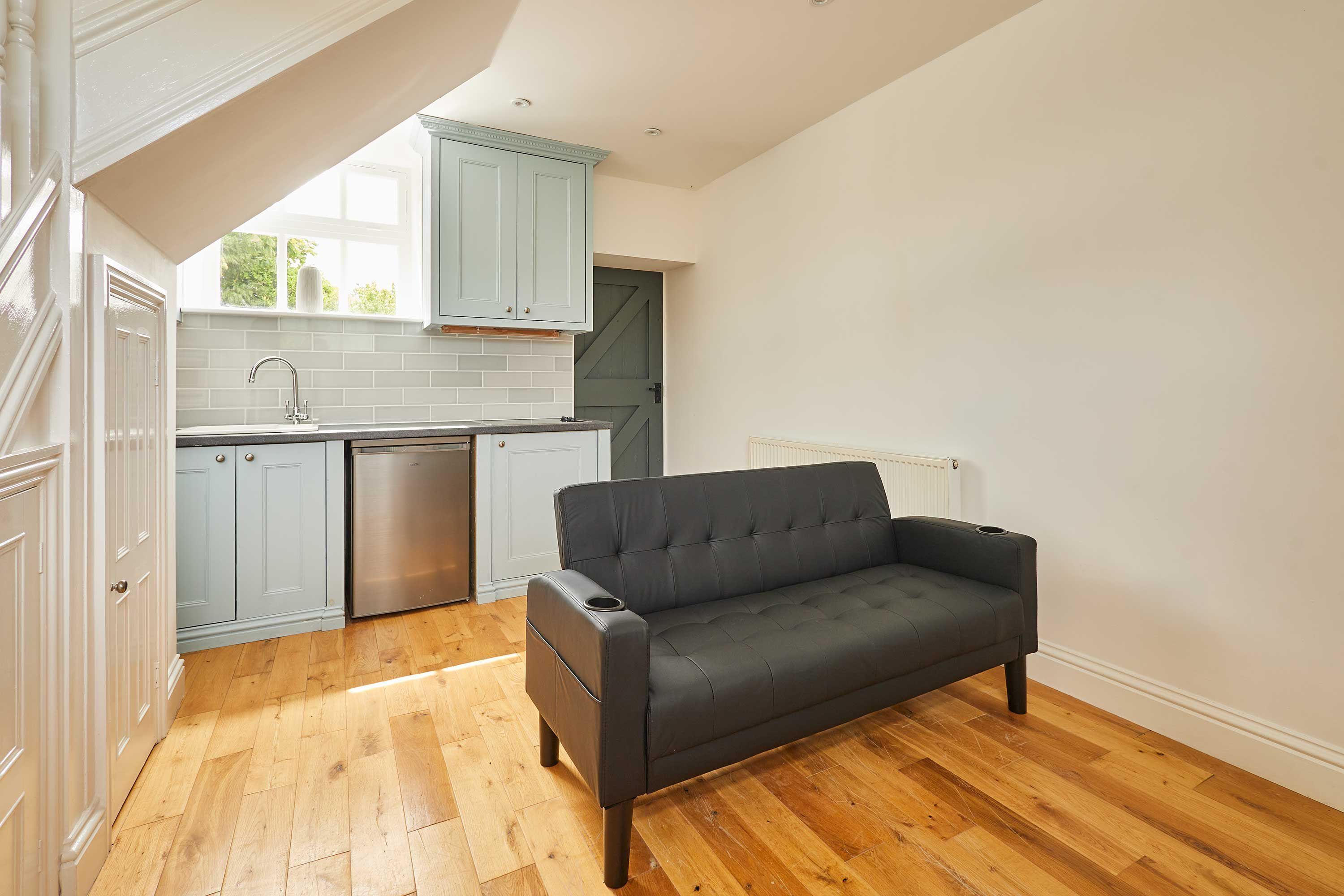 Una cocina moderna con armarios azul claro, un sofá gris y piso de madera.