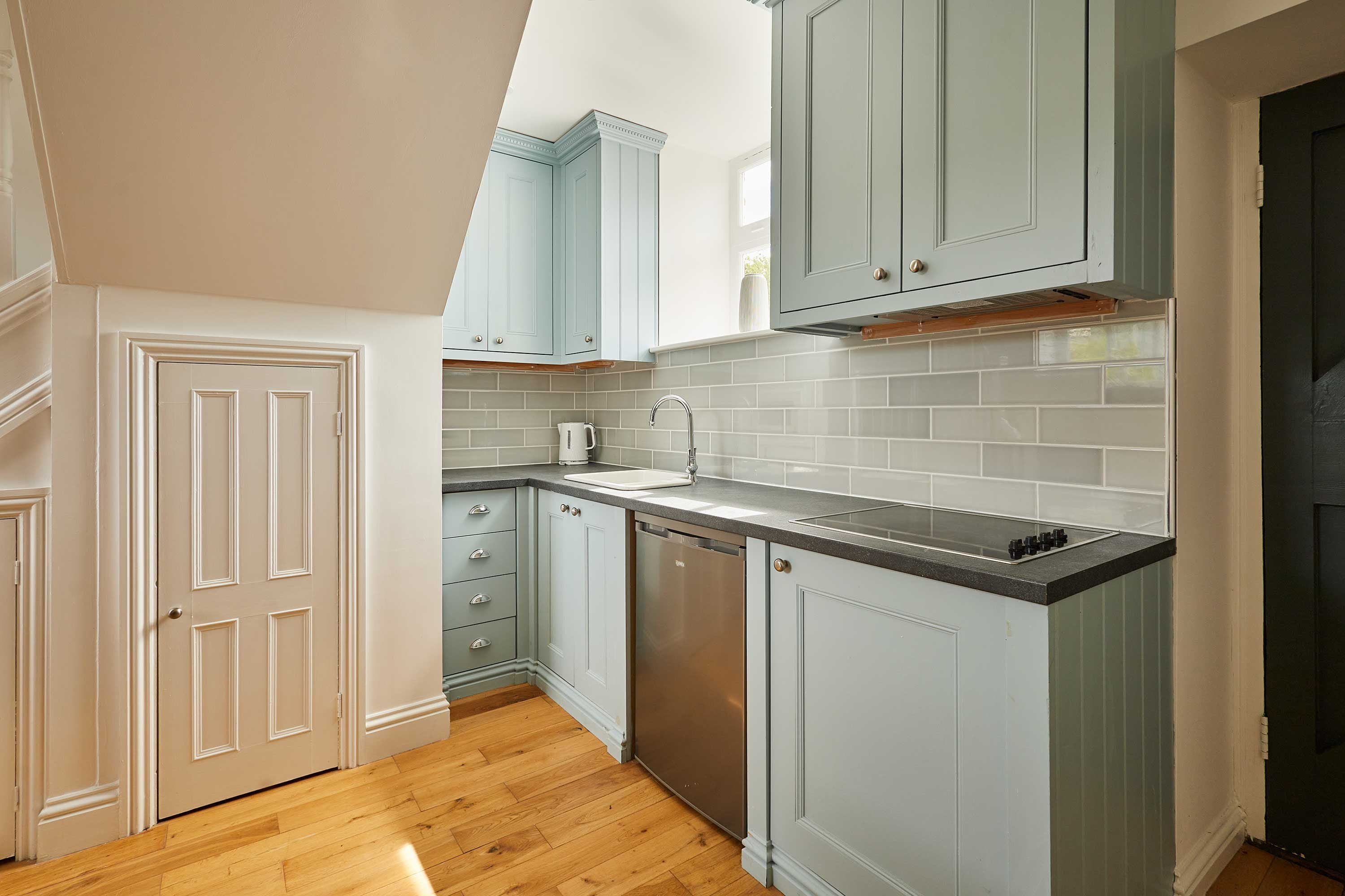 A kitchen with light blue cabinets, a dishwasher, and a wooden floor.
