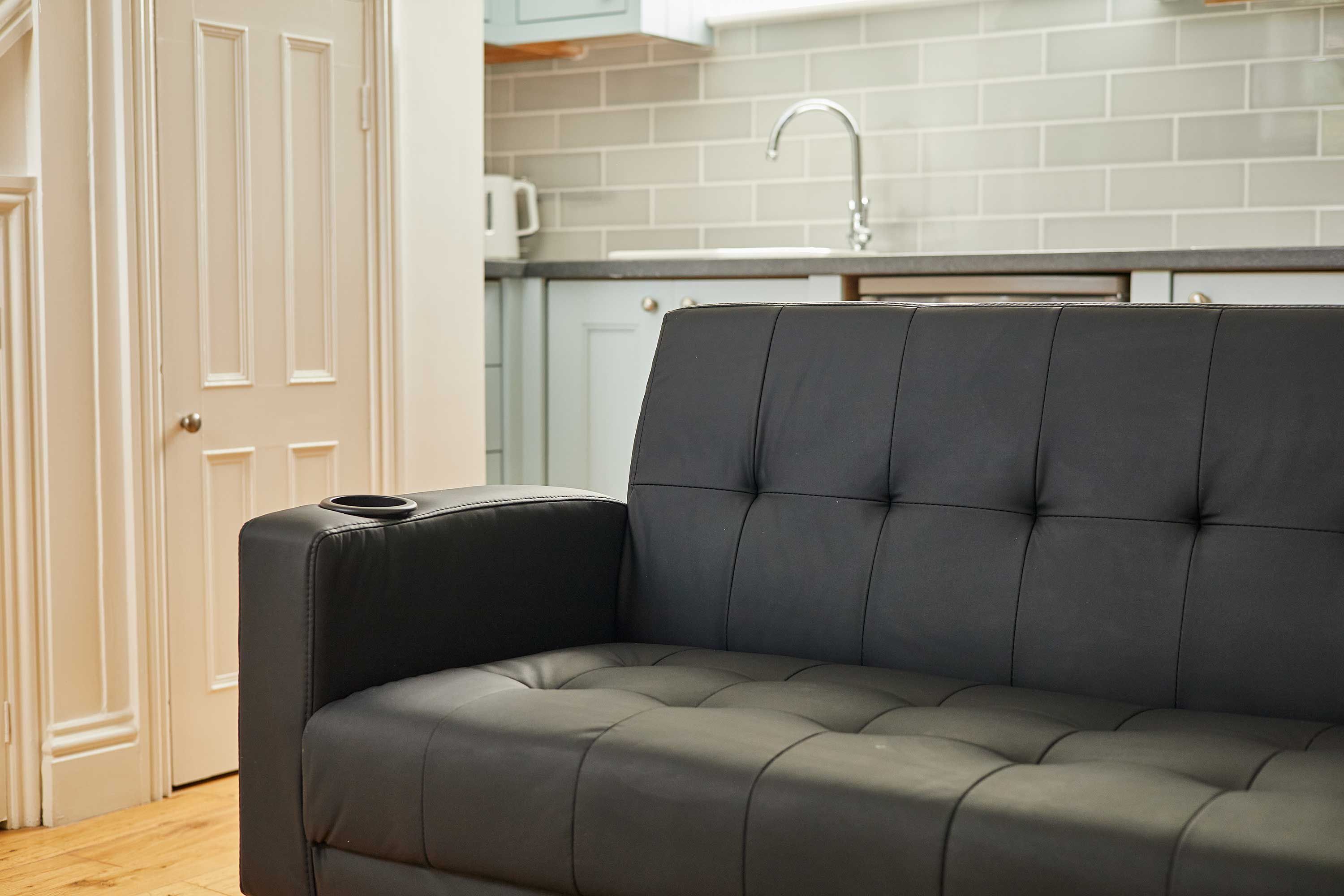 A modern kitchen with a black leather sofa, white cabinets, and a stainless steel sink.