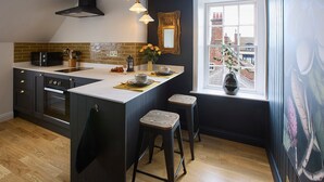 A modern kitchen with a large island, dark cabinetry, a black range hood, and a window with a city view. - Host Stay The Chimneys Whitby (Whitby)