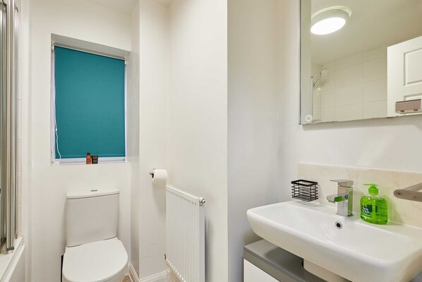 Une salle de bain comprenant des toilettes, un radiateur, un lavabo avec un miroir et une fenêtre avec un store bleu.