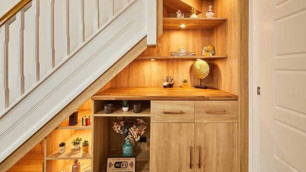 Una escalera de madera con barandilla blanca, estantes de madera con adornos y un mueble pequeño con cajones.