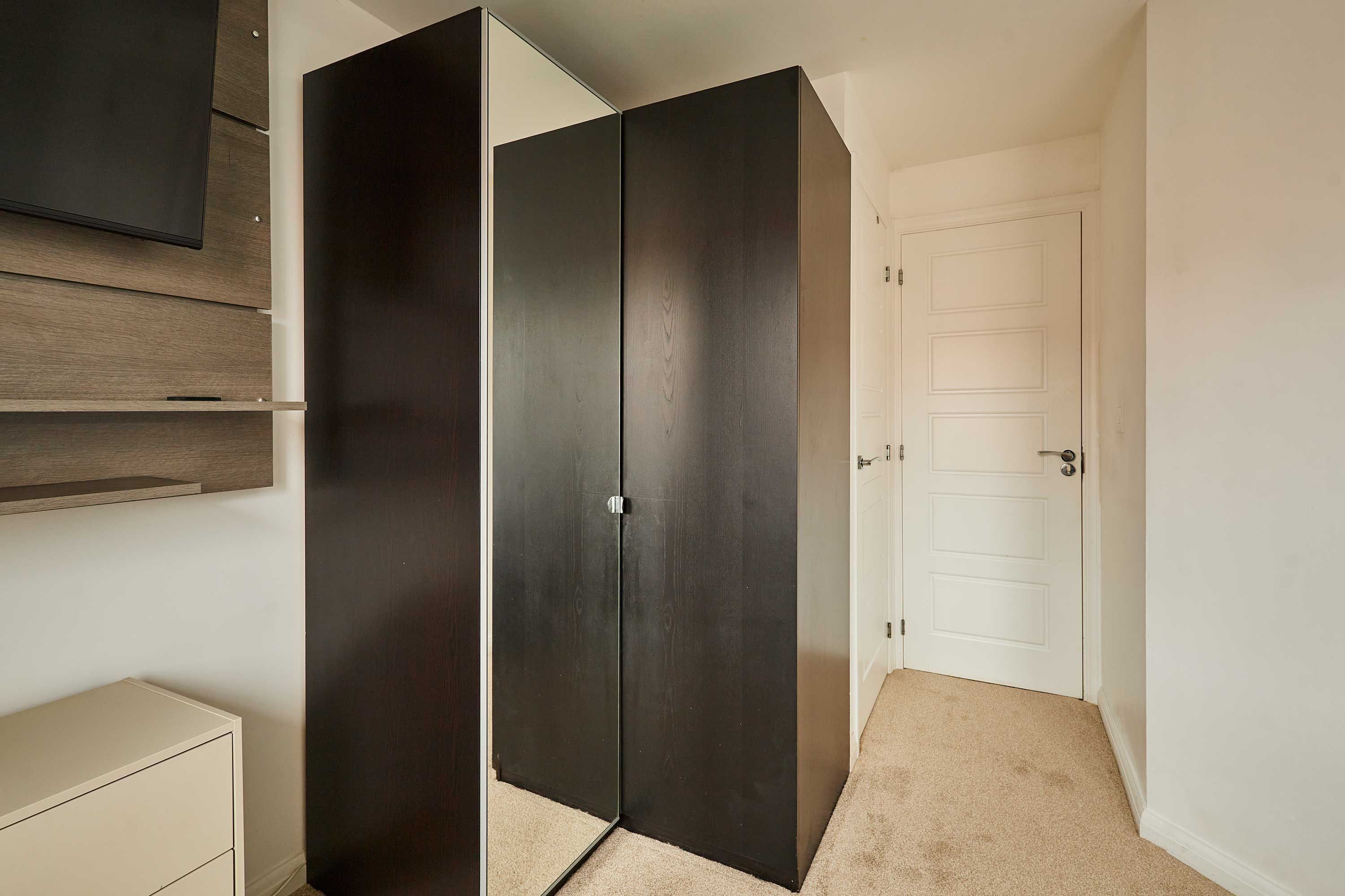 A room with a wardrobe, a door, and a wall-mounted shelf.