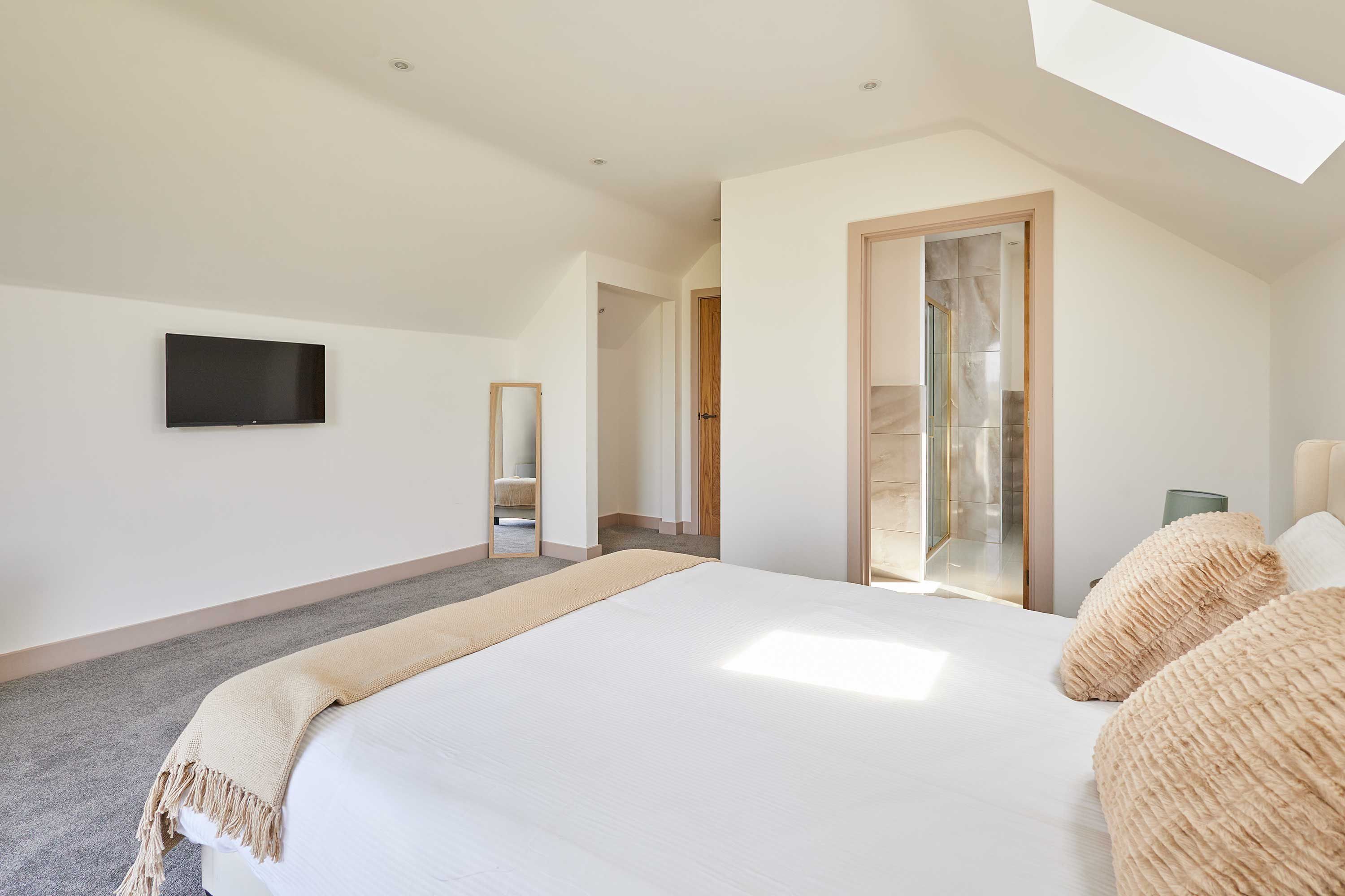 A bedroom with a large bed, a flat-screen TV, a mirror, and a door leading to a bathroom.