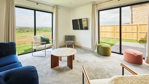 A spacious living room with large windows, a flat-screen TV, and a view of a wooden deck. - Host Stay Bluebell Cottage (Newcastle-upon-Tyne)