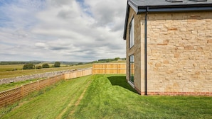 A modern building with stone walls and large windows, a sloped roof, and a grassy area with a wooden fence. - Host Stay Bluebell Cottage (Newcastle-upon-Tyne)
