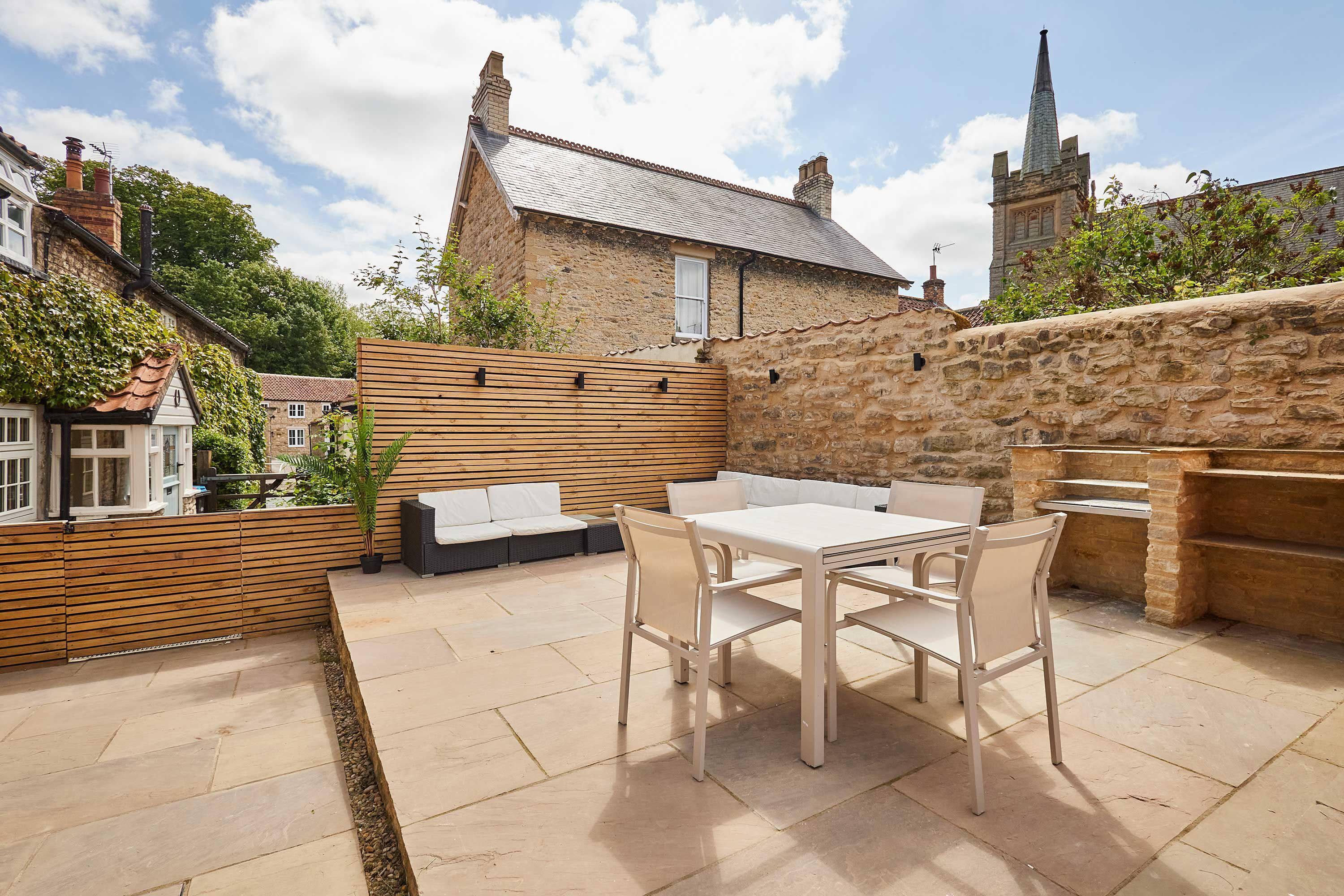 A patio with a table and chairs, a wooden fence, and a stone wall.