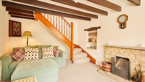 Un salon avec un escalier, une cheminée, un canapé vert et une horloge au mur.