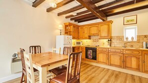 Une cuisine avec des meubles de rangement en bois, une table à manger, des chaises, un réfrigérateur, un four à micro-ondes et un lave-vaisselle.