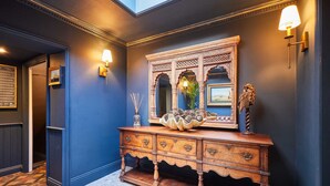 A hallway with a dark blue wall, a wooden console table with a mirror, and wall-mounted sconces. - Host Stay Topsail (Whitby)
