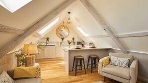 A loft-style room with a kitchen, wooden beams, a sofa, a coffee table, and a dining area. - Host Stay Topsail (Whitby)