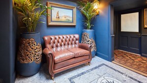 A lobby with a brown leather sofa, two large potted plants, a framed painting, and a patterned floor. - Host Stay Topsail (Whitby)