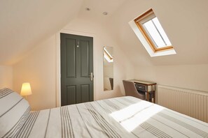 A bedroom with a bed, a desk, a chair, a lamp, a door, and a skylight.