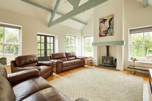 A spacious living room with a large brown leather sofa, a white rug, and a fireplace.