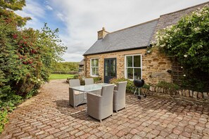 A stone house with a paved patio, outdoor furniture, and a view of the surrounding greenery.