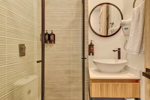 A bathroom with a glass shower door, a round mirror, a white sink, and toiletries on the wall. - w Enchanting Loft in the Heart of Chico Norte (Bogotá)