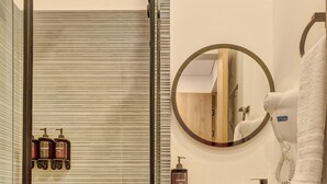 Un baño moderno con cabina de ducha de vidrio, un espejo redondo grande, un lavabo blanco y un mueble de tocador de madera.