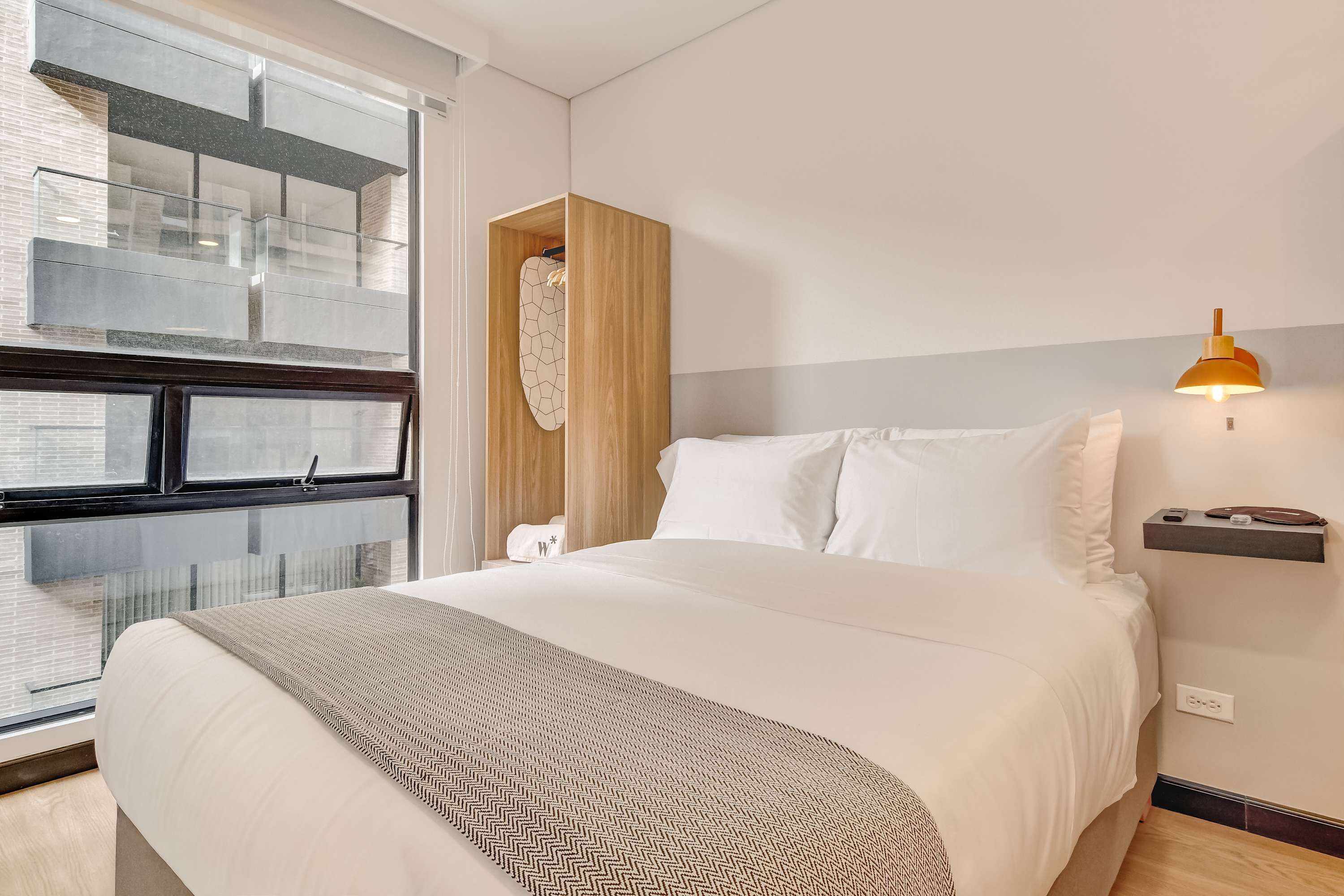 Ein Hotelzimmer mit einem großen Bett, einem Holzschrank, einem Nachttisch mit Lampe und einem Fenster mit Blick auf die Stadt.