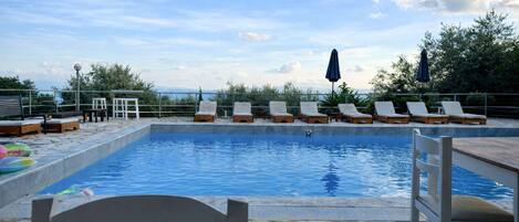A swimming pool with lounge chairs and umbrellas, surrounded by stone tiles and greenery.
