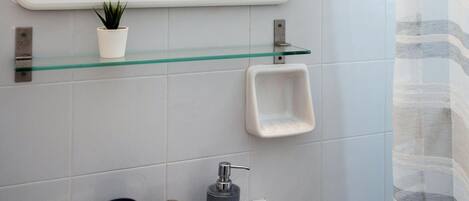 A bathroom with a white sink, a glass shelf with a potted plant, a mirror, and a shower curtain.