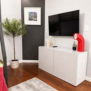 Ein modernes Wohnzimmer mit einem weißen Schrank, einem flachbildfernseher an der Wand, einer Topfpflanze und einem gerahmten Bild.