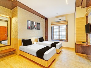 Ein Hotelzimmer mit zwei Betten, einem großen Spiegel, einem Fenster mit Jalousien und einer fest installierten Klimaanlage.