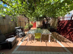 Une terrasse avec une table et des chaises en verre, entourée d’une clôture en bois et agrémentée de plantes en pot.