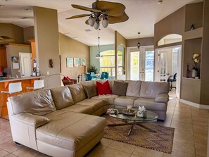 A living room with a sectional sofa, a glass coffee table, and a ceiling fan. - Villa Vito, Gulf Access, Pool, Dock & Office (Cape Coral)