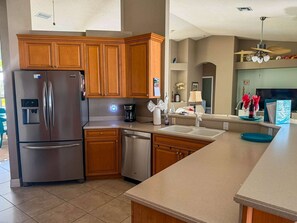A modern kitchen with wooden cabinets, stainless steel appliances, and a large island with a sink. - Villa Vito, Gulf Access, Pool, Dock & Office (Cape Coral)