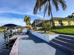 A waterfront property with a dock, a covered outdoor seating area, and a building with a sloped roof. - Villa Vito, Gulf Access, Pool, Dock & Office (Cape Coral)