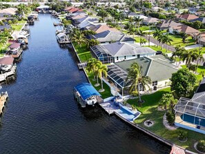 A residential area with a canal, houses with solar panels, and a boat docked at the canal's edge. - Villa Vito, Gulf Access, Pool, Dock & Office (Cape Coral)