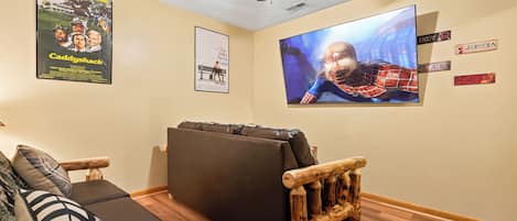 Una habitación con ventilador de techo, televisor de pantalla plana grande, sofá y una silla de madera.