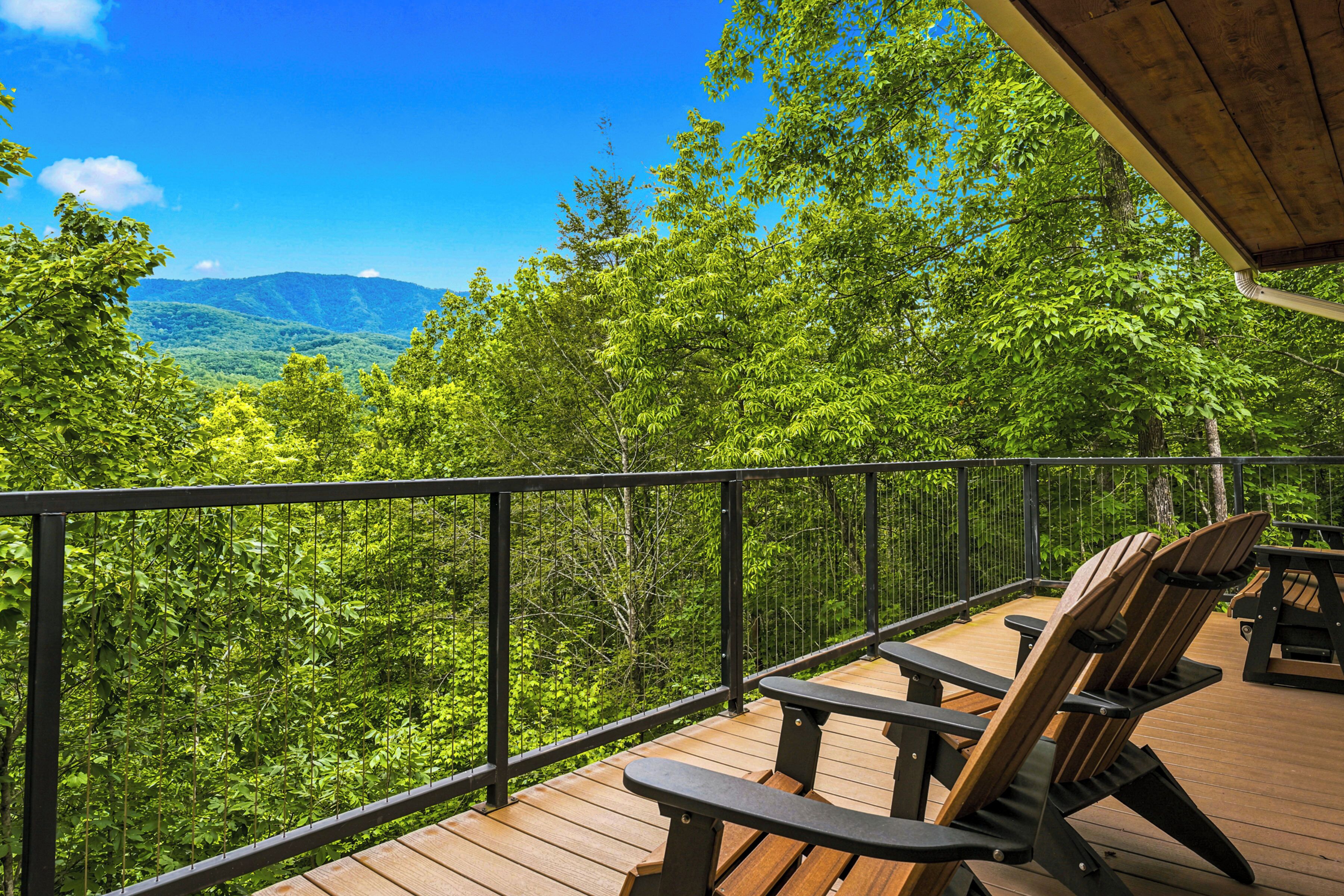 Une terrasse dotée de chaises et de tables en bois, offrant une vue sur un paysage boisé avec des montagnes à l’horizon.