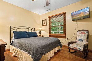 A bedroom with a bed, a chair, a lamp, a window with blinds, a television, and a picture on the wall. - Mountain Views, Hot Tub, Pool Access (Gatlinburg)
