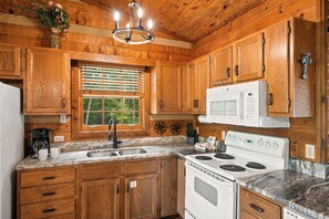 A wooden cabin kitchen with a stove, sink, and a microwave. - Mountain Views, Hot Tub, Pool Access (Gatlinburg)