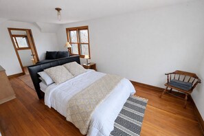 Ein Schlafzimmer mit einem Bett, einem Nachttisch, einer Lampe, einem Sessel und einem Fenster.