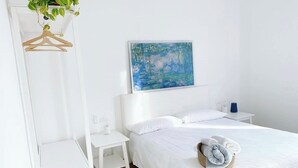 A hotel room with a bed, a nightstand, a hanging plant, a painting, and a towel on the bed.