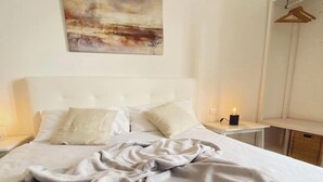 A neatly made bed with a blanket, a bedside table with a candle, and a painting on the wall.